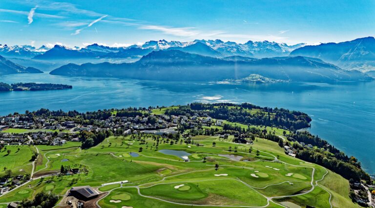 Golfers playing on a lush green course at Golf Meggen in Switzerland, with rolling fairways and views of Lake Lucerne and surrounding mountains in the background.