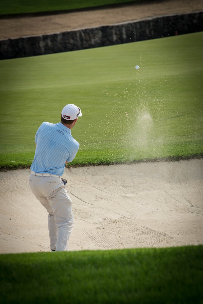 Golfer swinging from sand trap on a sunny day at the golf course.